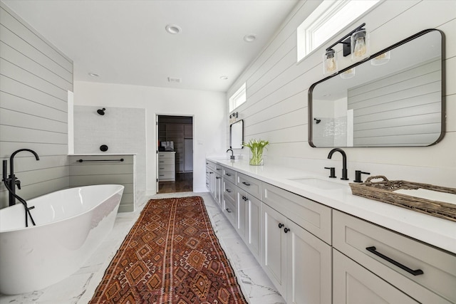 bathroom with a soaking tub, wooden walls, marble finish floor, and a sink