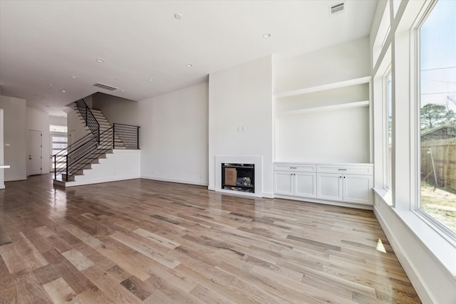 unfurnished living room with stairs, light wood-style floors, a fireplace, and visible vents