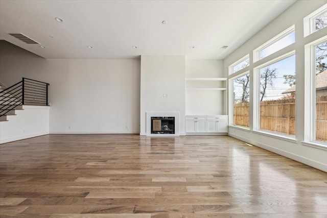 unfurnished living room featuring light wood-type flooring, visible vents, stairs, and a fireplace