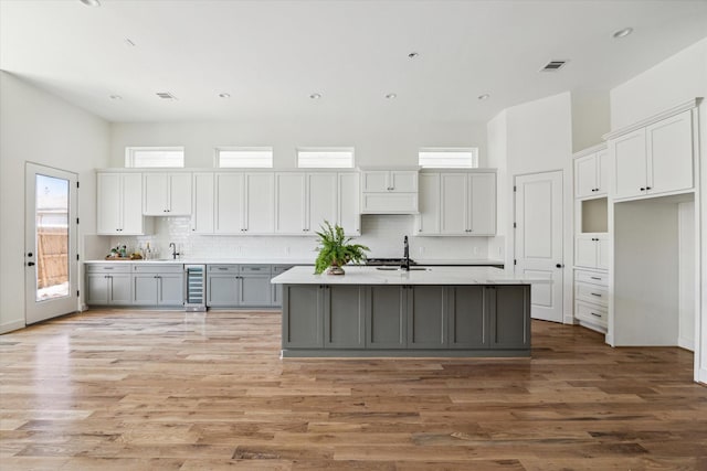 kitchen with visible vents, a center island with sink, gray cabinets, a sink, and wine cooler