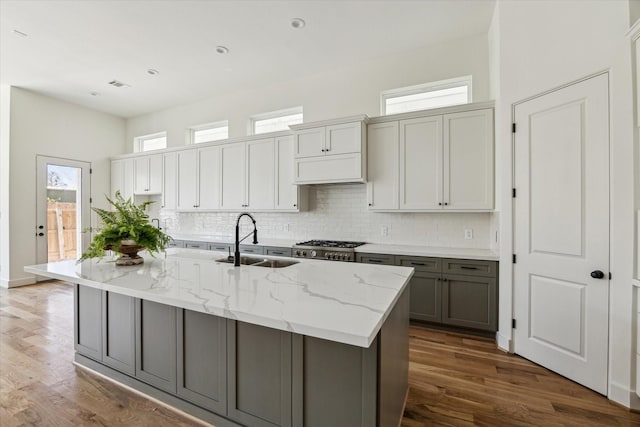 kitchen with wood finished floors, light stone countertops, gray cabinetry, a sink, and backsplash