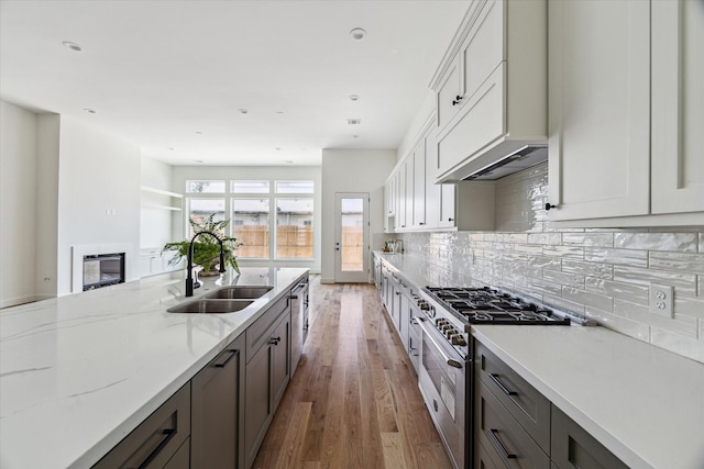 kitchen with high end stainless steel range, a sink, wood finished floors, decorative backsplash, and light stone countertops