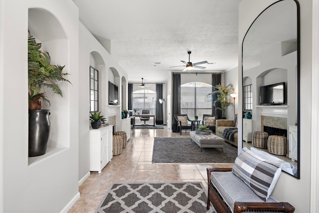 living room with baseboards, ceiling fan, light tile patterned floors, a fireplace, and a textured ceiling