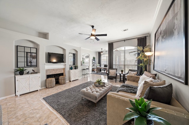 tiled living area with a ceiling fan, baseboards, visible vents, a fireplace, and a textured ceiling