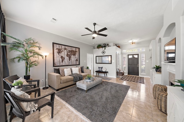 living area with light tile patterned floors, baseboards, visible vents, arched walkways, and crown molding