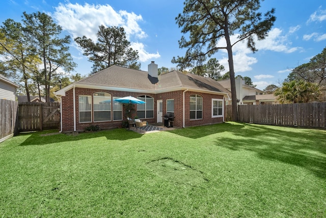 back of property featuring a lawn, a fenced backyard, brick siding, and a chimney