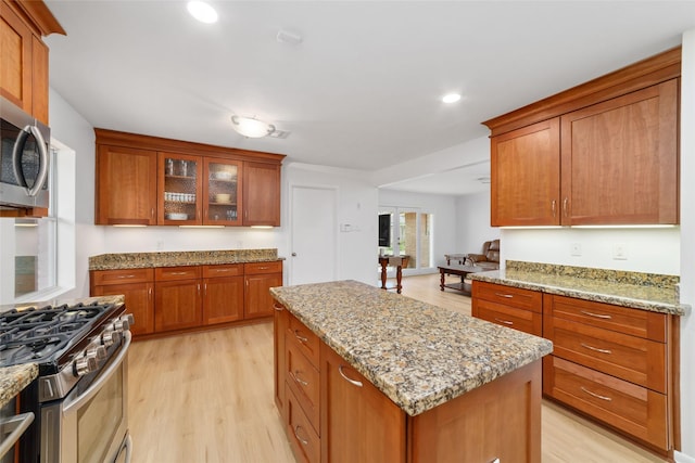 kitchen featuring light stone counters, brown cabinetry, light wood finished floors, a kitchen island, and appliances with stainless steel finishes