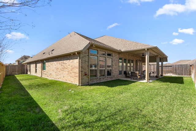 rear view of property with a fenced backyard, a yard, a patio, and roof with shingles