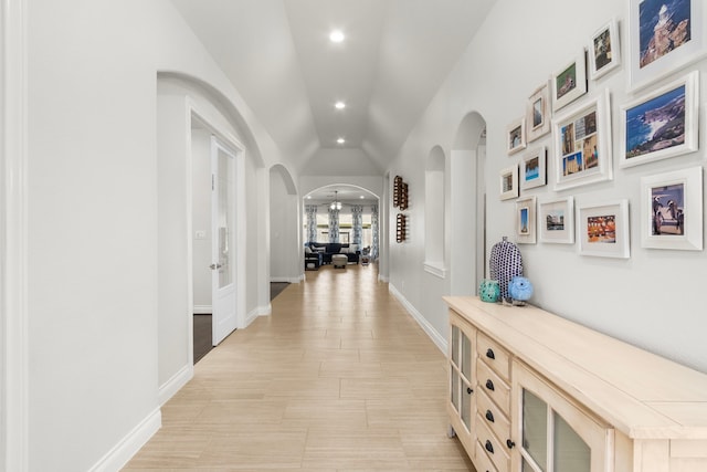 corridor featuring arched walkways, recessed lighting, baseboards, and lofted ceiling