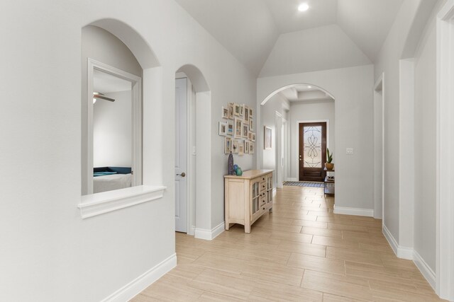 hallway with lofted ceiling, arched walkways, baseboards, and wood finish floors