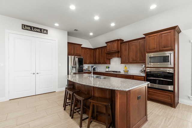 kitchen featuring a kitchen bar, a sink, light stone counters, tasteful backsplash, and stainless steel appliances