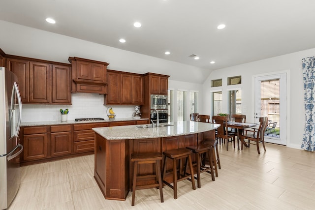 kitchen with a sink, a kitchen breakfast bar, backsplash, appliances with stainless steel finishes, and light stone countertops