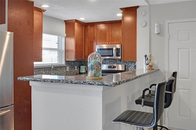 kitchen with stainless steel appliances, backsplash, a breakfast bar, and dark stone counters