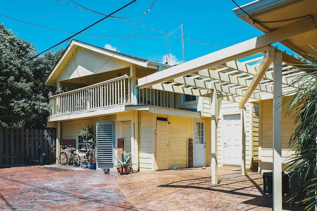 back of property with a pergola, a balcony, and fence