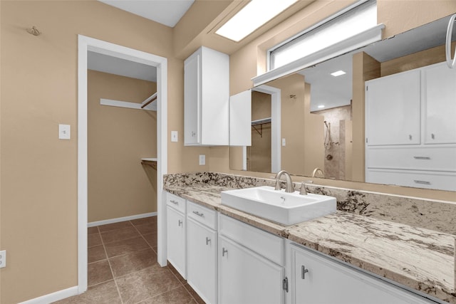 full bathroom featuring vanity, baseboards, walk in shower, a walk in closet, and tile patterned floors