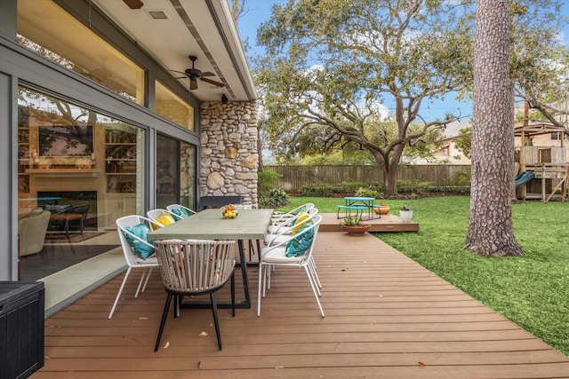 deck with a lawn, a playground, fence, outdoor dining area, and ceiling fan