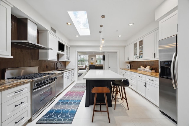 kitchen with glass insert cabinets, appliances with stainless steel finishes, a skylight, white cabinets, and wall chimney exhaust hood