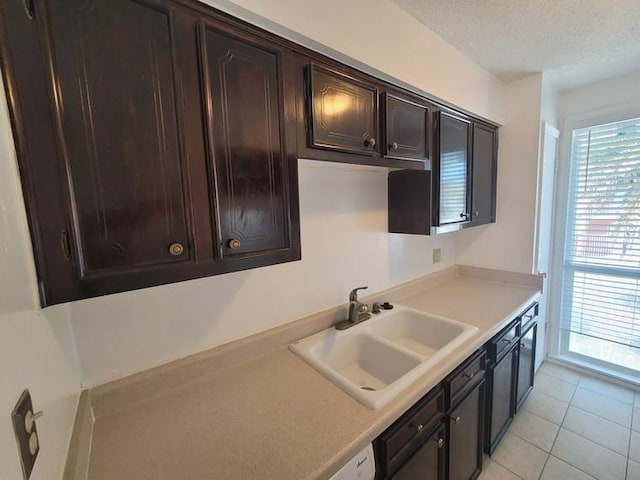 kitchen featuring dark brown cabinetry, light countertops, light tile patterned floors, a textured ceiling, and a sink