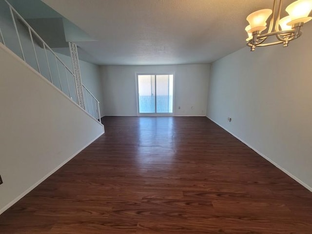 unfurnished room featuring stairs, baseboards, an inviting chandelier, and dark wood-style flooring