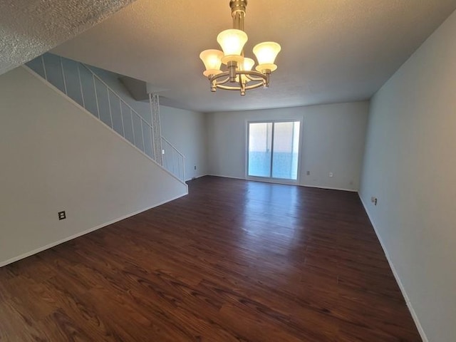 spare room with a chandelier, a textured ceiling, stairs, and dark wood-style flooring