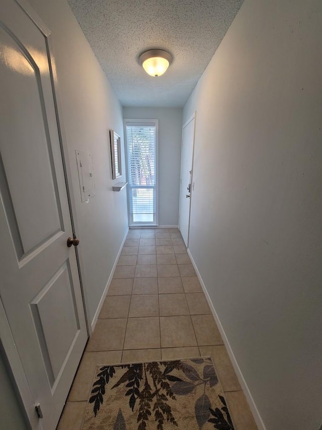 corridor featuring light tile patterned floors, a textured ceiling, and baseboards