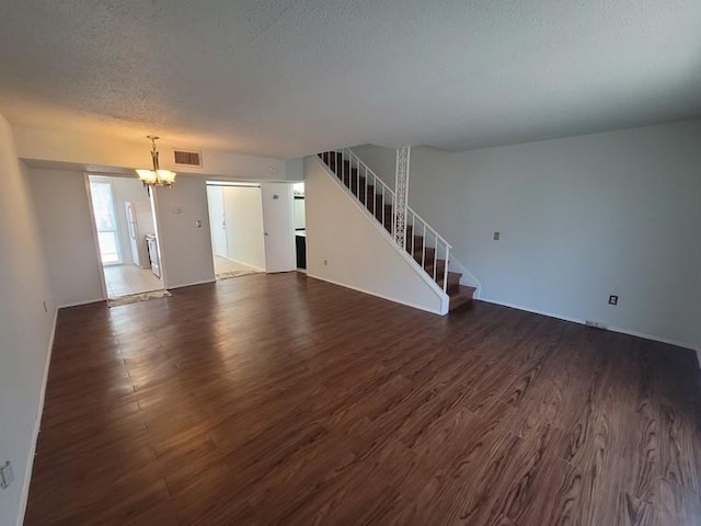 unfurnished living room with visible vents, an inviting chandelier, stairs, dark wood-type flooring, and a textured ceiling