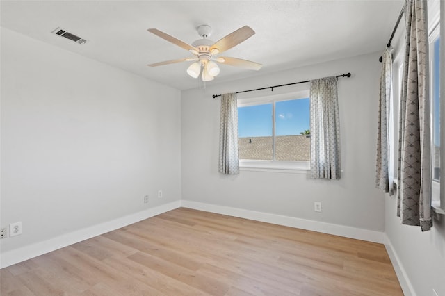 unfurnished room with a ceiling fan, wood finished floors, visible vents, and baseboards