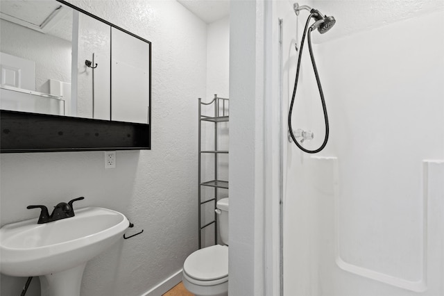 bathroom featuring walk in shower, toilet, a textured wall, and a sink