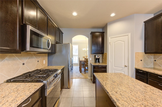 kitchen featuring arched walkways, dark brown cabinetry, appliances with stainless steel finishes, and light stone countertops