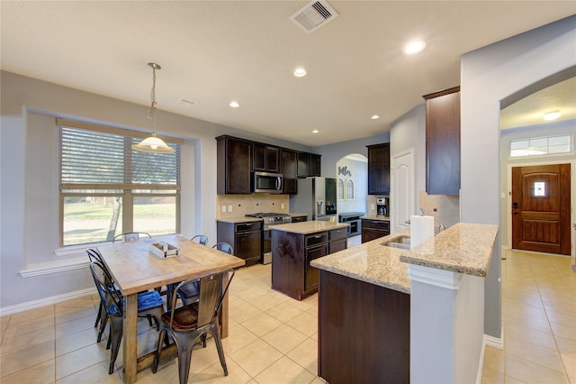 kitchen with a sink, a kitchen island, arched walkways, appliances with stainless steel finishes, and dark brown cabinets