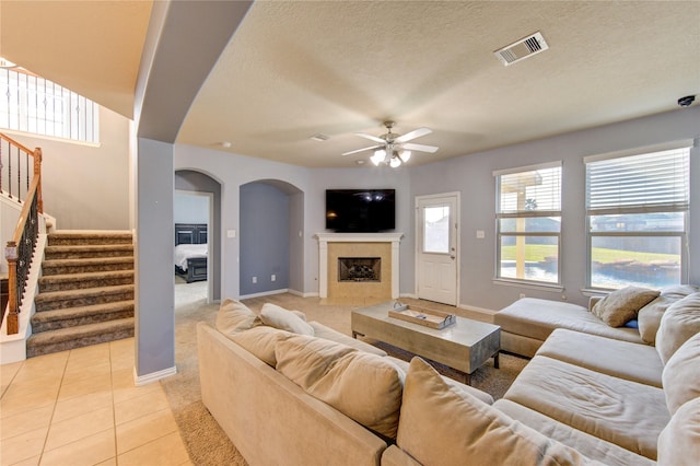 living room featuring light tile patterned floors, visible vents, arched walkways, ceiling fan, and stairs