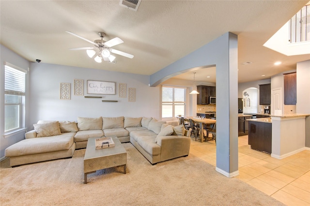 living room featuring light tile patterned floors, visible vents, arched walkways, ceiling fan, and light carpet