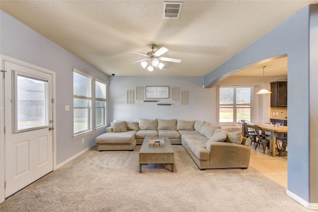 tiled living room featuring a ceiling fan, carpet, visible vents, arched walkways, and a textured ceiling