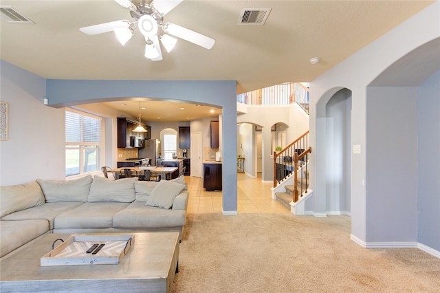 living area with visible vents, light colored carpet, arched walkways, and ceiling fan