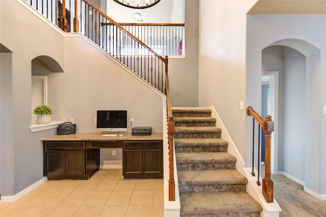 stairs with tile patterned flooring, a high ceiling, baseboards, and arched walkways