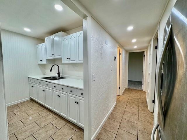 kitchen featuring a sink, freestanding refrigerator, white cabinets, light countertops, and a textured wall