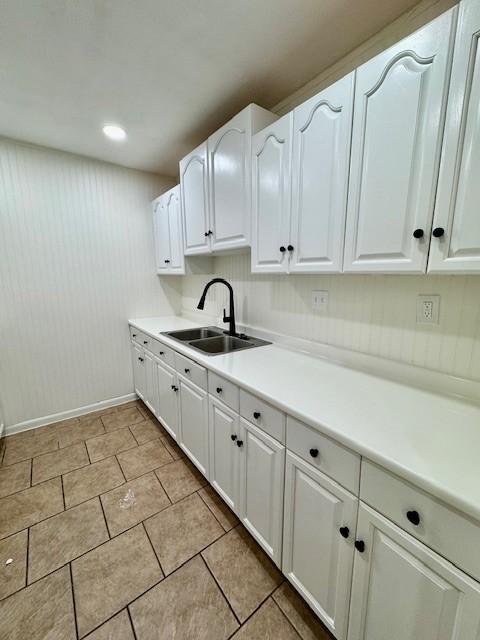 kitchen with baseboards, light countertops, light tile patterned flooring, white cabinets, and a sink