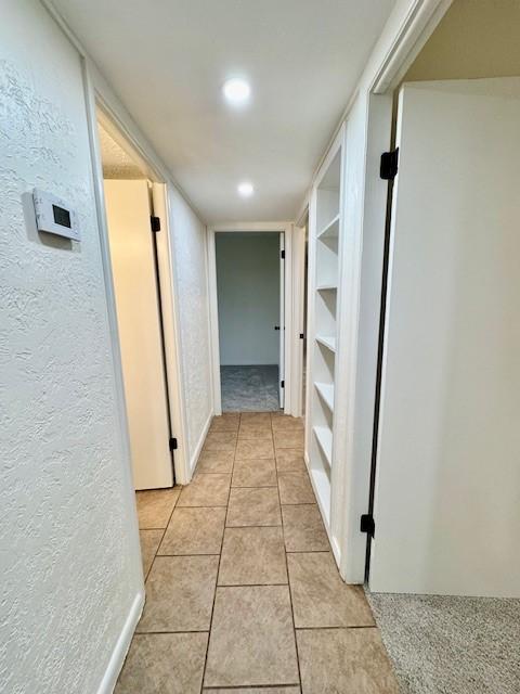 hallway featuring light tile patterned floors and a textured wall