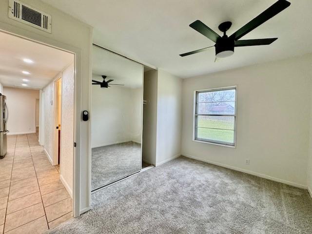 unfurnished bedroom with light carpet, visible vents, freestanding refrigerator, and a closet