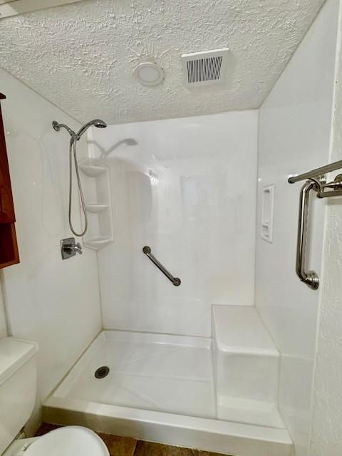 bathroom with a stall shower, toilet, visible vents, and a textured ceiling