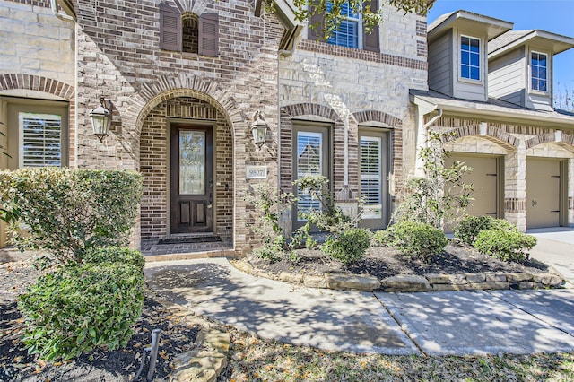 doorway to property with concrete driveway, an attached garage, brick siding, and stone siding