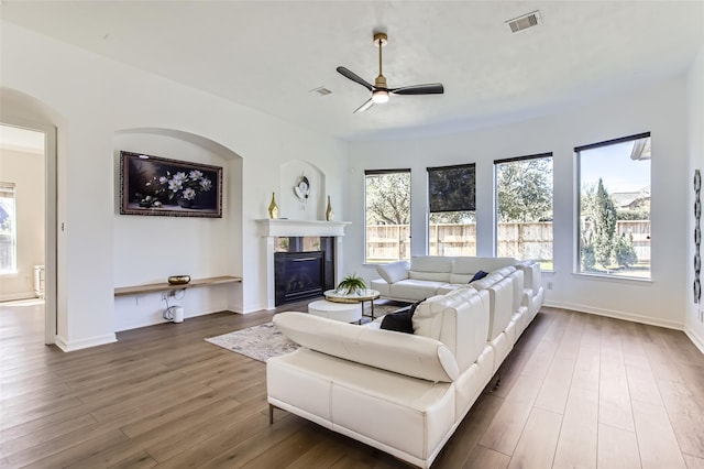 living room featuring a glass covered fireplace, visible vents, wood finished floors, and a ceiling fan