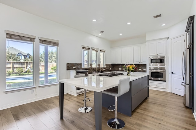 kitchen with visible vents, a kitchen island, white cabinetry, appliances with stainless steel finishes, and decorative backsplash