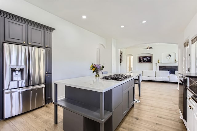 kitchen featuring a kitchen island, a fireplace, a kitchen breakfast bar, arched walkways, and stainless steel appliances