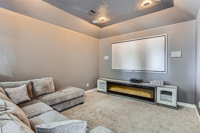 carpeted cinema with visible vents, lofted ceiling, baseboards, and a glass covered fireplace