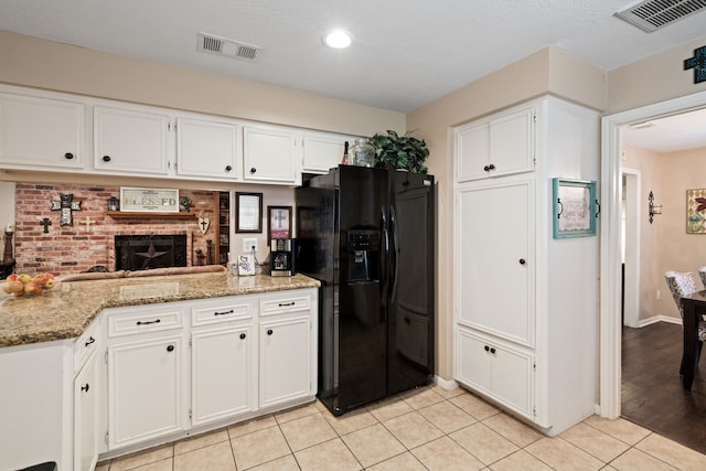 kitchen with light tile patterned floors, black fridge with ice dispenser, white cabinetry, and visible vents