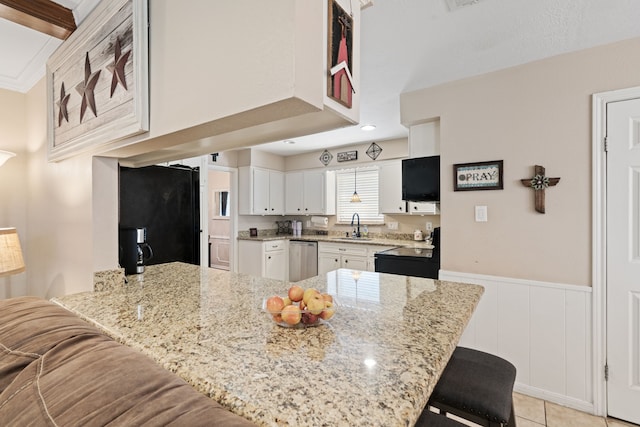 kitchen with a breakfast bar, a peninsula, black appliances, wainscoting, and white cabinetry