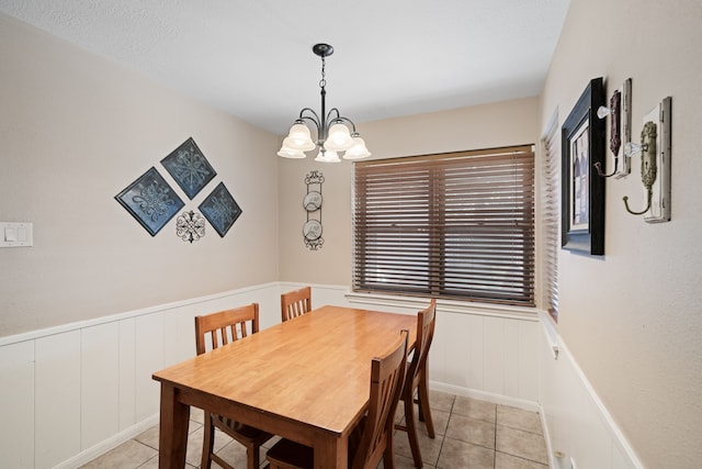 dining area with light tile patterned floors, a wainscoted wall, and an inviting chandelier