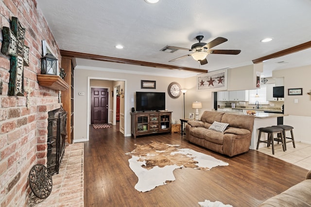 living area with a brick fireplace, brick wall, ornamental molding, light wood-style flooring, and a ceiling fan