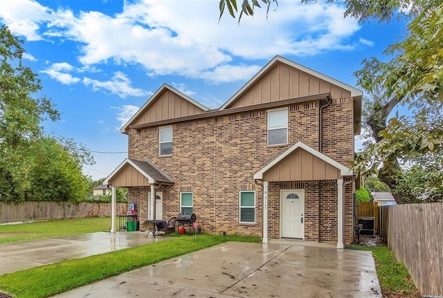 view of front of house with a fenced backyard, board and batten siding, a front yard, brick siding, and a patio area